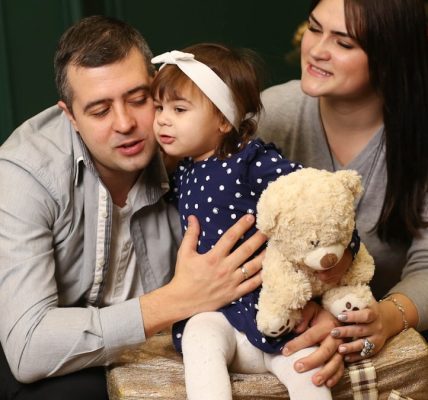 a man, woman and child sitting in front of a christmas tree